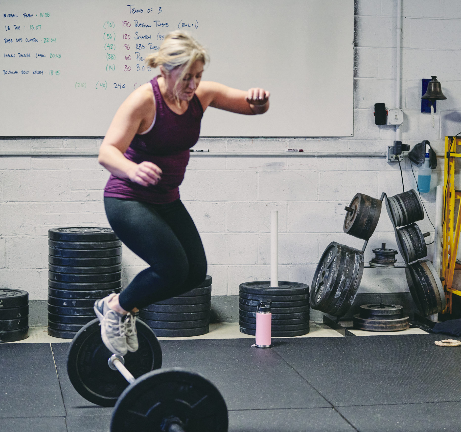 A woman is jumping in the air while holding onto a barbell.